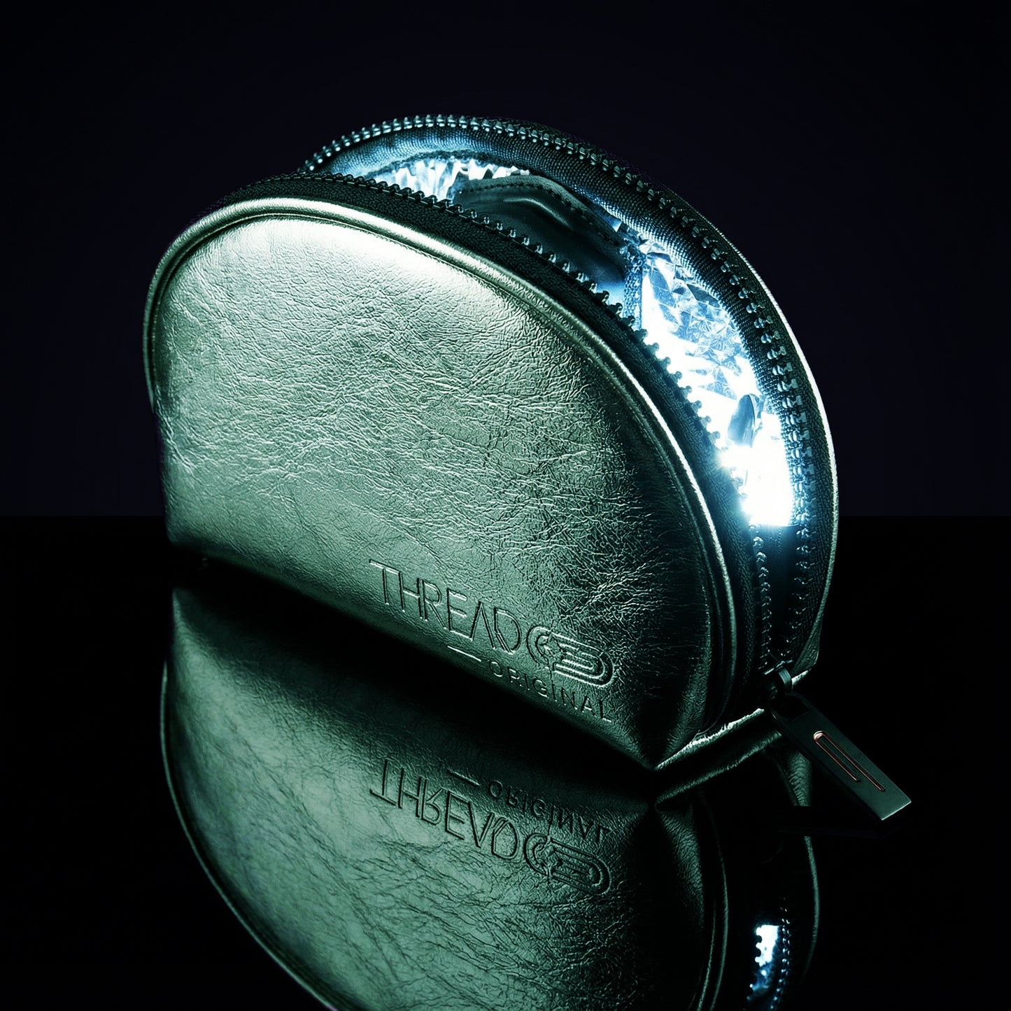 Mint green metallic LED makeup bag with illuminated interior on reflective black surface. Compact vegan leather cosmetic pouch with rechargeable light and wipeable insulated lining by Thread Original.