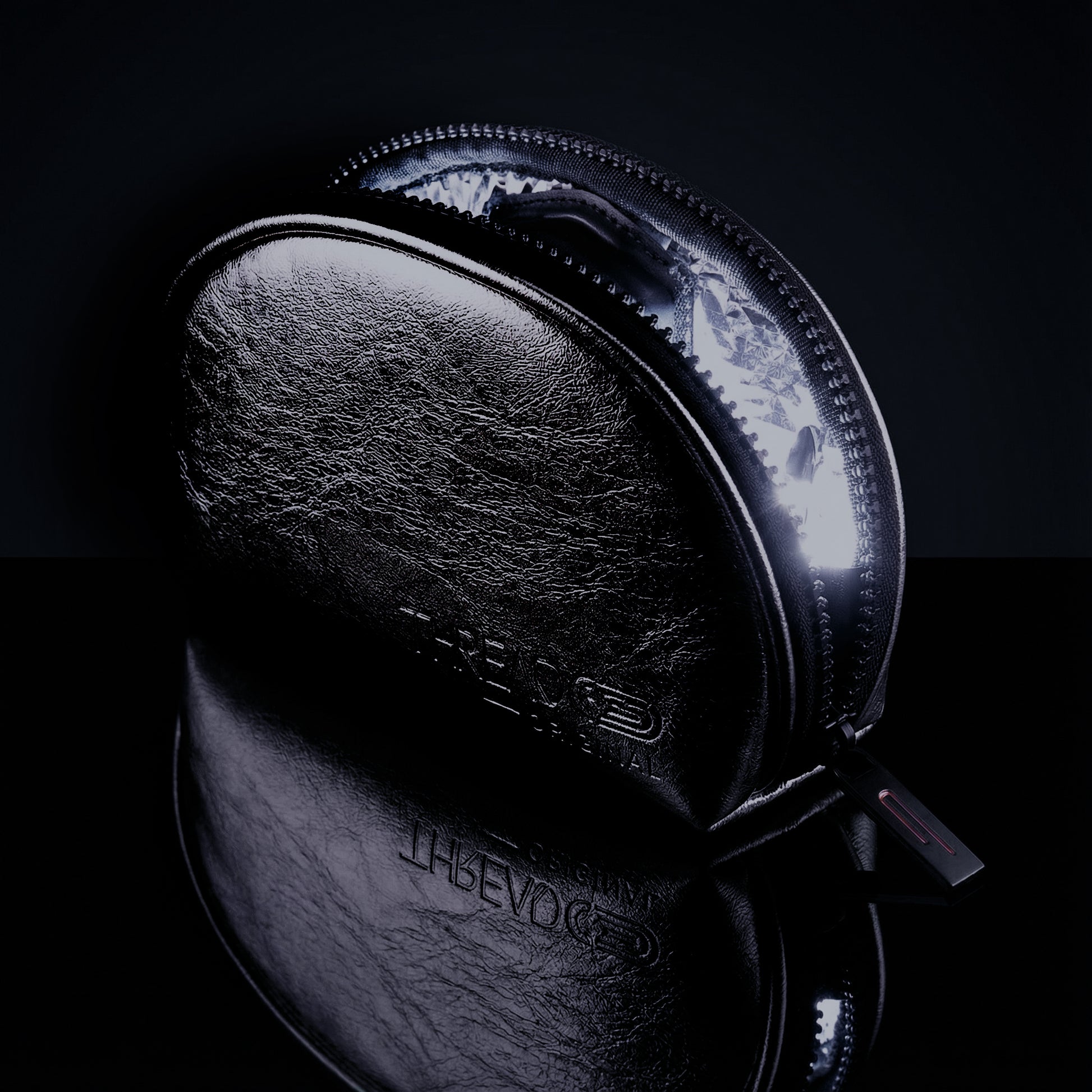 Onyx black metallic LED makeup bag with illuminated interior on reflective black surface. Compact vegan leather cosmetic pouch with rechargeable light and wipeable insulated lining by Thread Original.