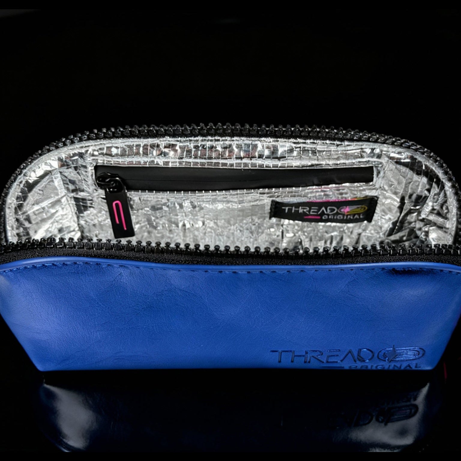 Ocean blue metallic compact makeup bag with wipeable insulated interior on reflective black surface. Slim vegan leather cosmetic pouch by Thread Original.