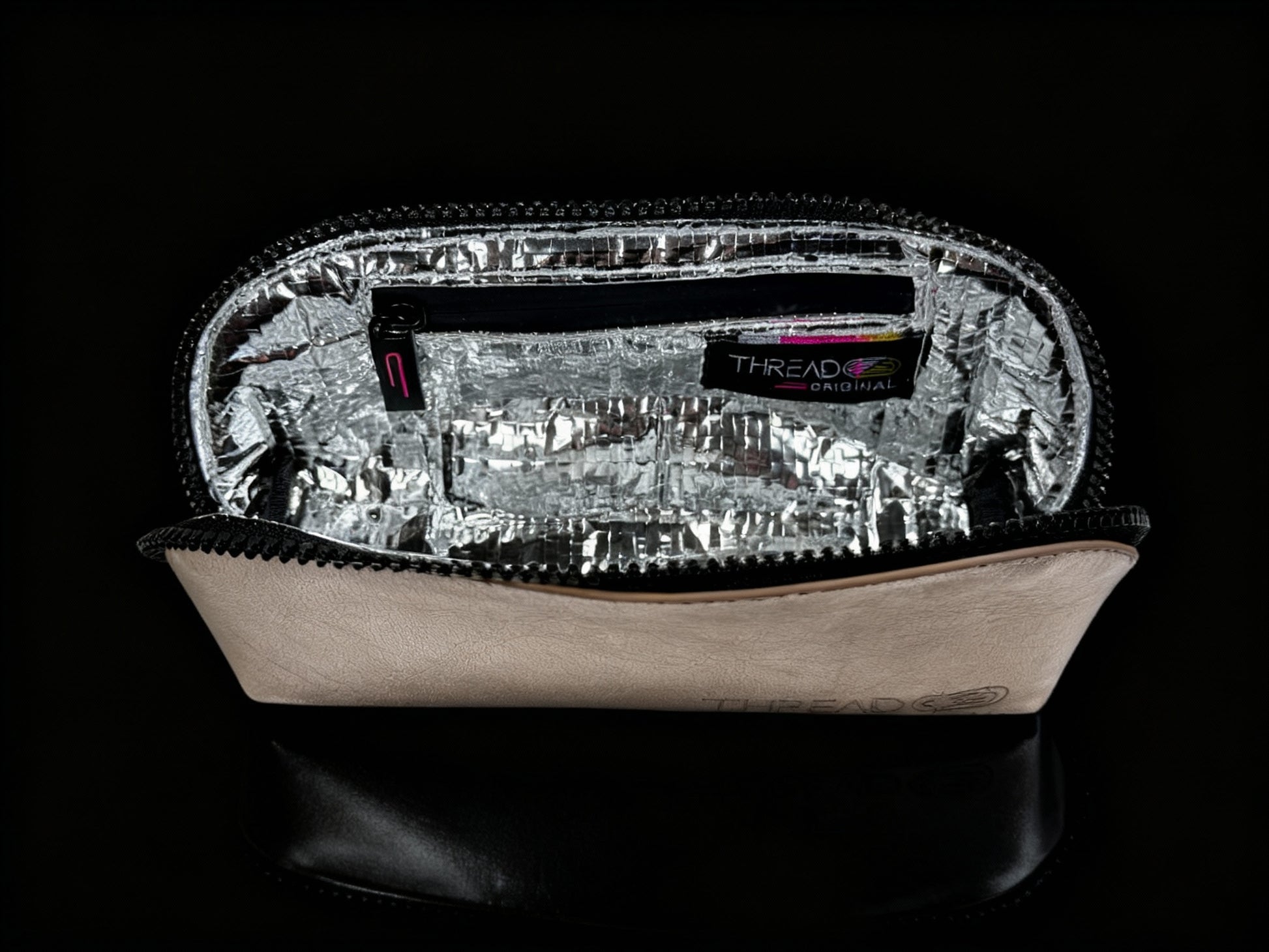 Champagne metallic compact makeup bag with wipeable insulated interior on reflective black surface. Slim vegan leather cosmetic pouch by Thread Original.
