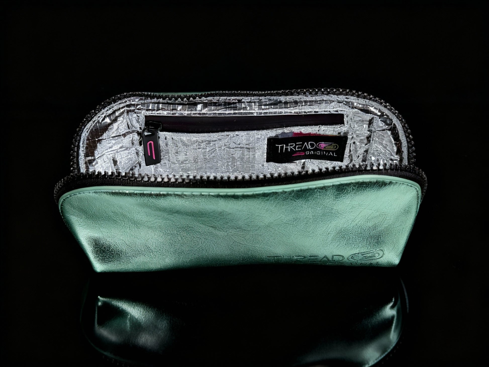 Mint green metallic compact makeup bag with wipeable insulated interior on reflective black surface. Slim vegan leather cosmetic pouch by Thread Original.