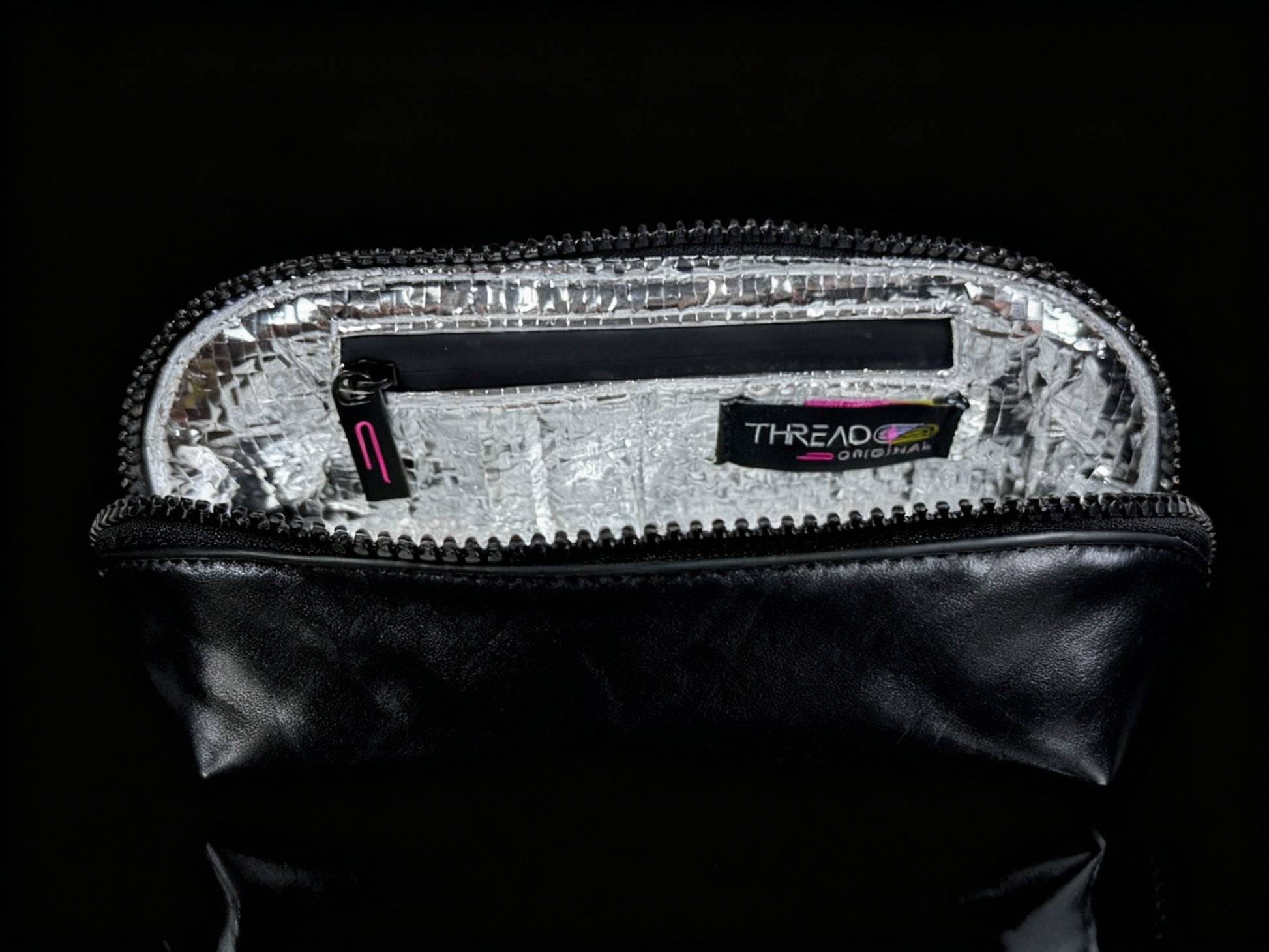 Onyx black metallic compact makeup bag with wipeable insulated interior on reflective black surface. Slim vegan leather cosmetic pouch by Thread Original.